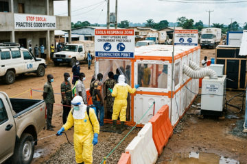 People lined up at Ebola disinfection station with health workers in protective suits spraying disinfectant