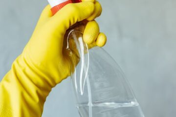gloved hand holding cleaning spray bottle